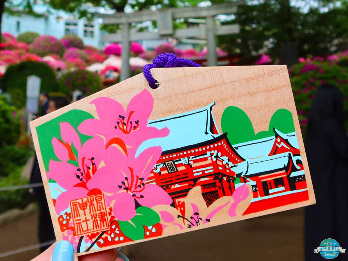 A wooden ema wishing plaque painted with azaleas and Nezu Shrine, held up at the Azalea Festival in Tokyo