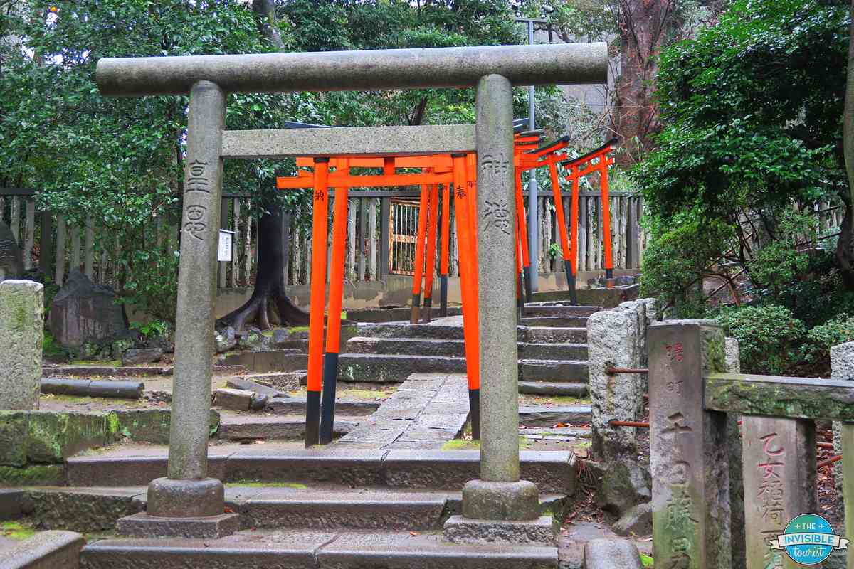 A stone torii in front of the vermilion torii gates of Otome Inari Shrine at Nezu Shrine, Tokyo, on a rainy day